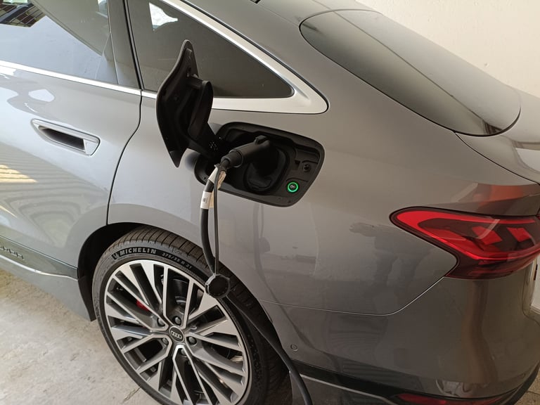 Puerto de carga abierto en el costado de un auto plateado mostrando el conector del cable